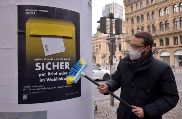 Stadtrat Schneider bringt ein Plakat der Kampagne „Frankfurt wählt sicher“ an